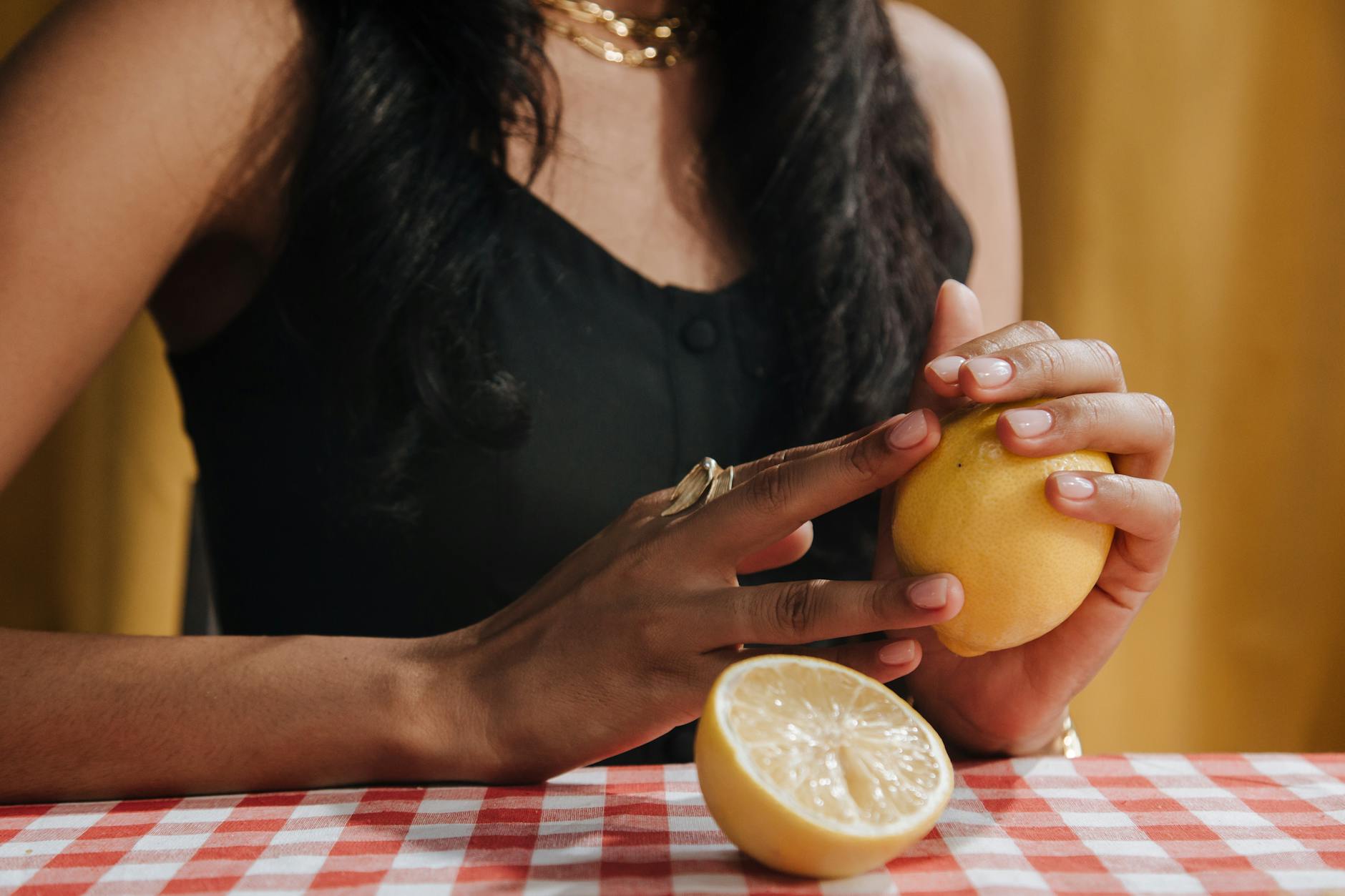 A close-up of a woman holding a fresh lemon at a dining table, symbolizing restored sensation and natural vitality.