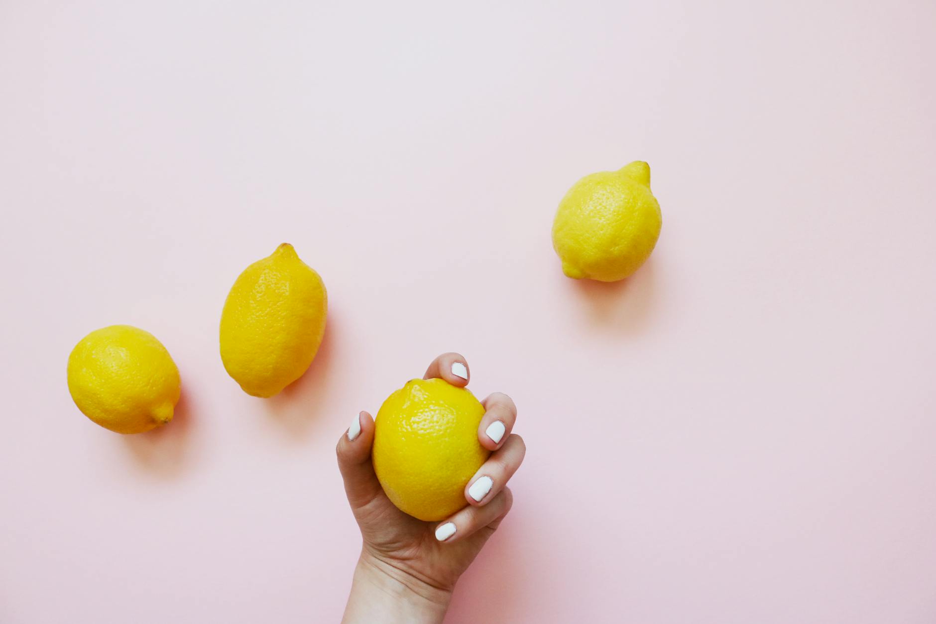 A hand holding a bright lemon on a soft pink background, symbolizing renewed sensation and pleasure