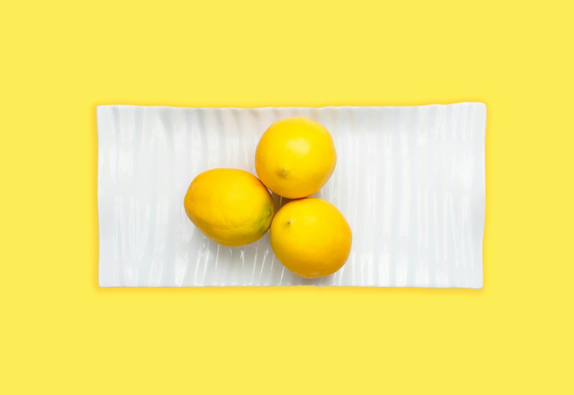 Fresh lemons arranged on a white plate with vibrant yellow background, symbolizing renewed sensitivity and natural pleasure
