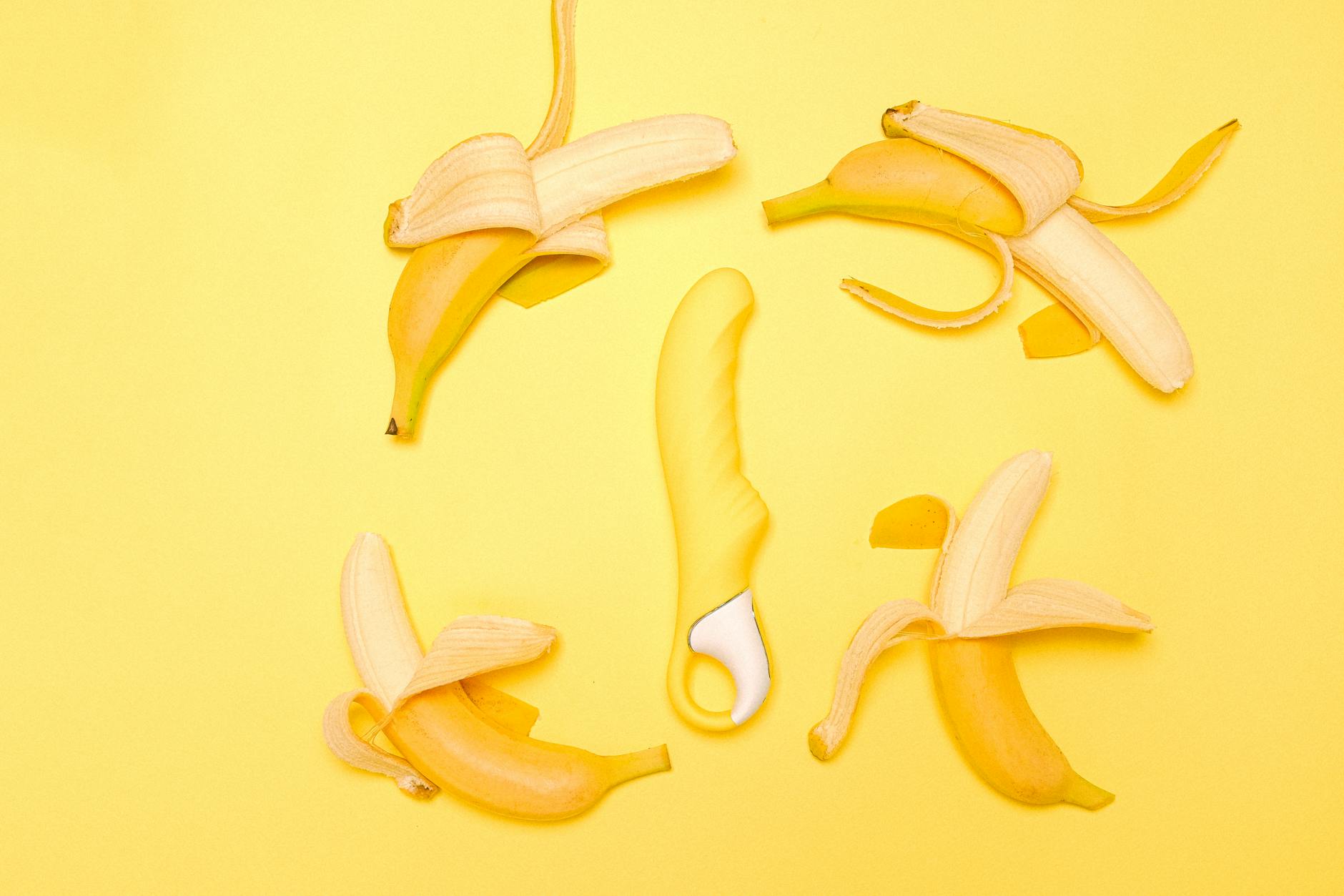 Creative flat lay of a yellow silicone lemon clitoral vibrator surrounded by peeled lemons on a bright yellow background.