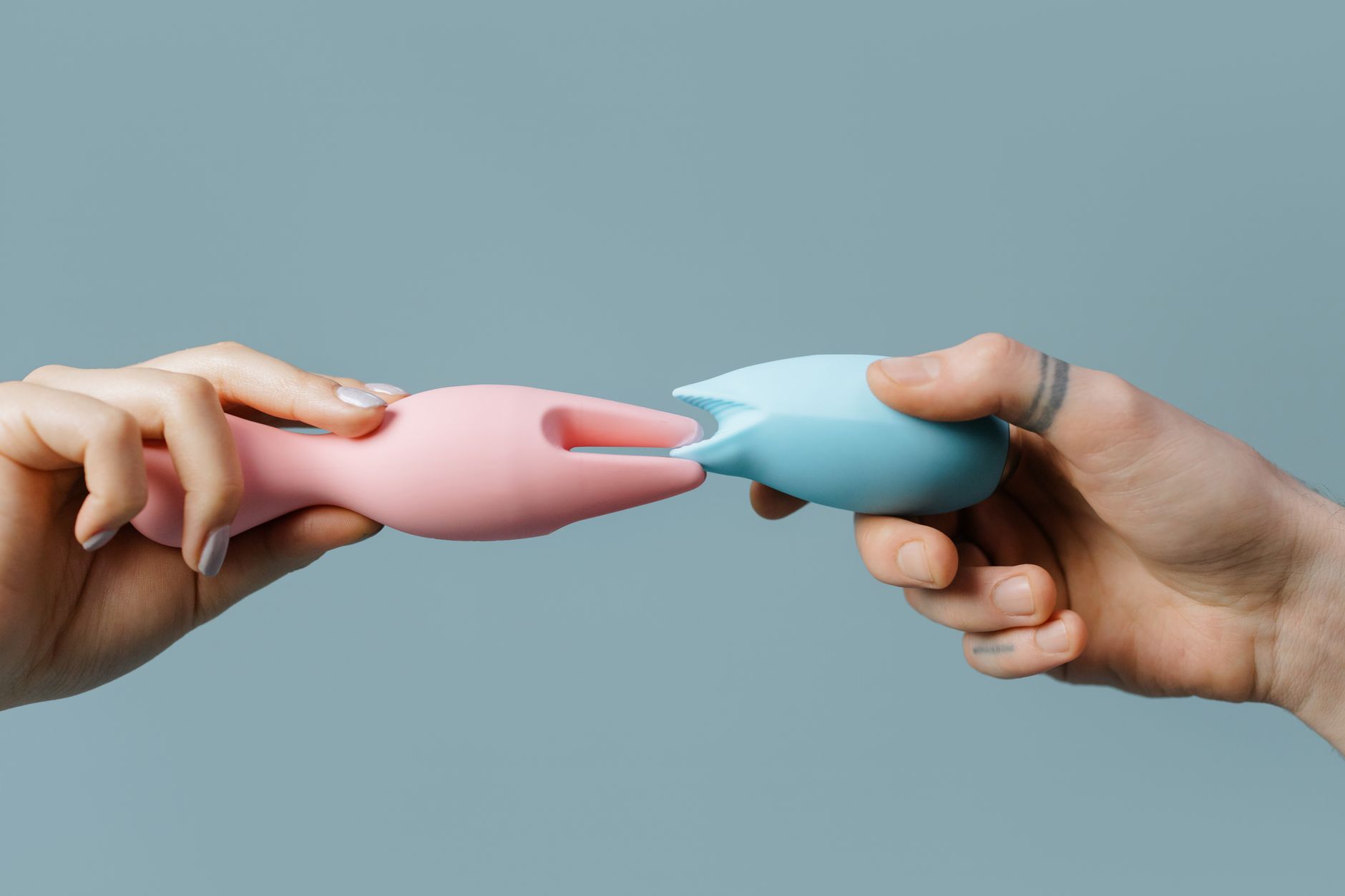 Femme portant des lunettes tenant deux vibromasseurs colorés contre un fond violet