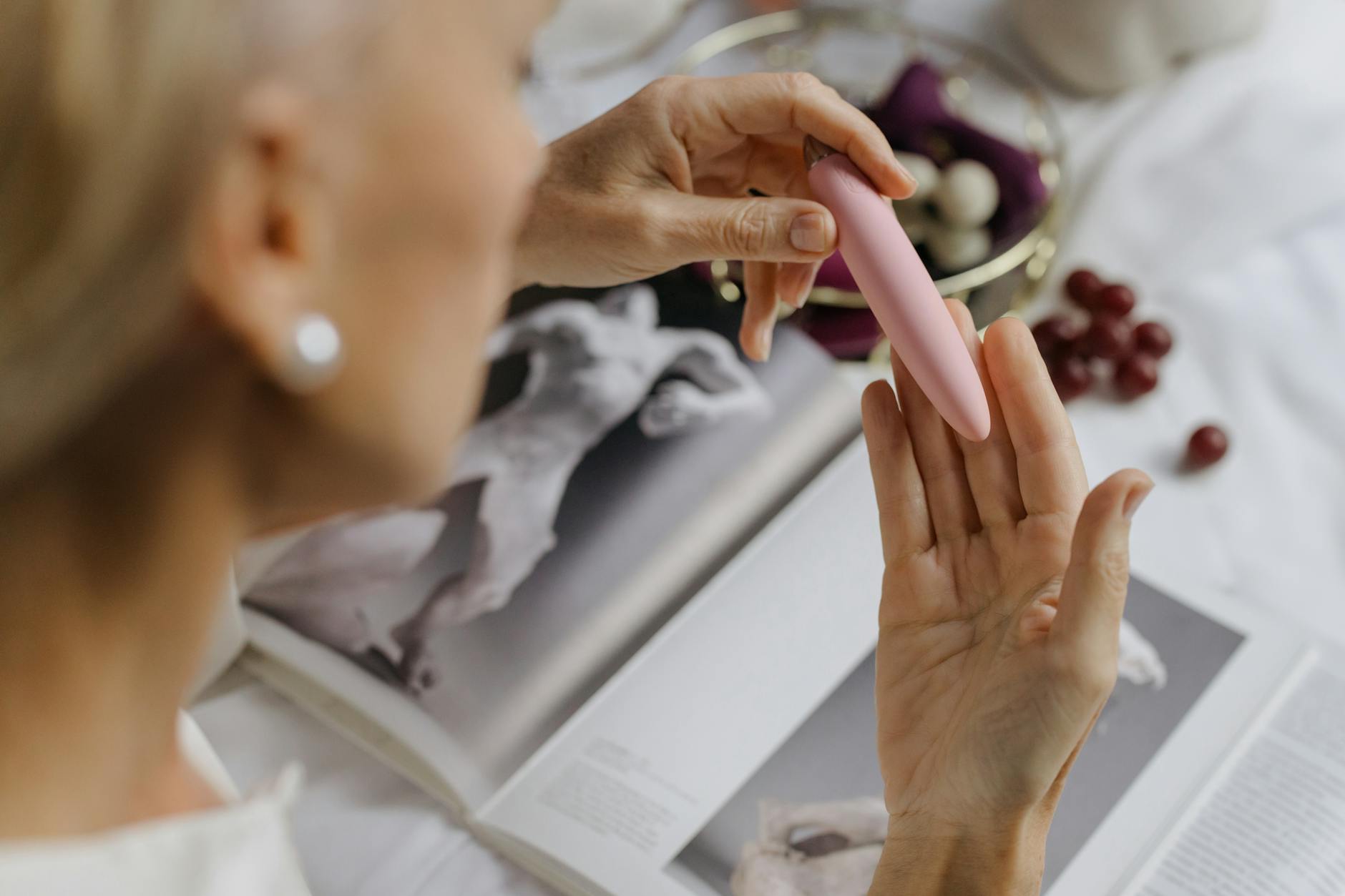 Close-up of a woman holding a pink vibrator with art books in soft focus, emphasizing intimate solo exploration.