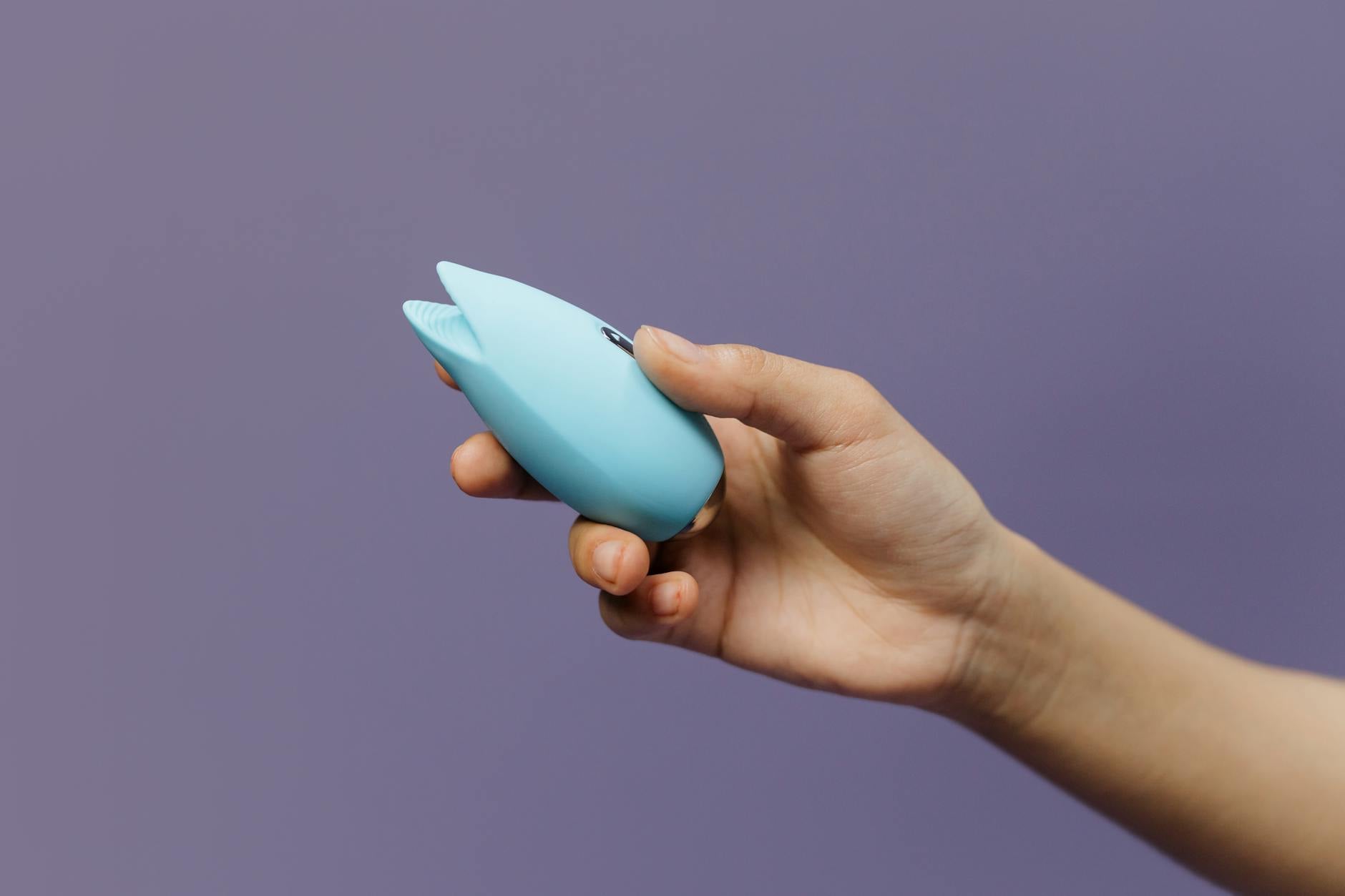A hand holding a blue silicone lemon vibrator against a purple background