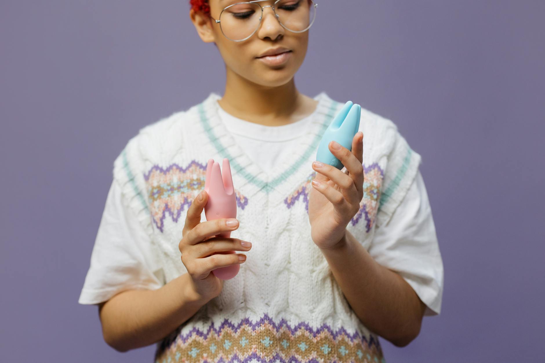 Woman with eyeglasses holding colorful vibrators in a contemplative manner.