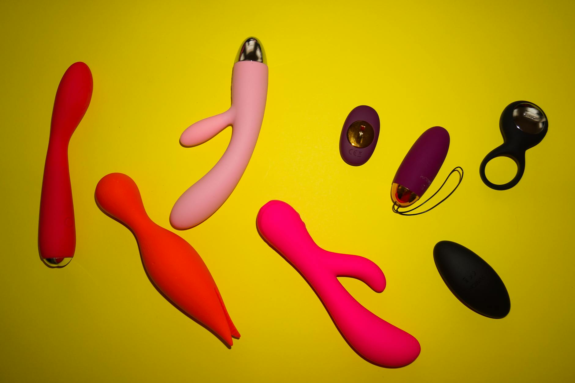 Vibrant collection of colorful sex toys arranged on a bright yellow surface